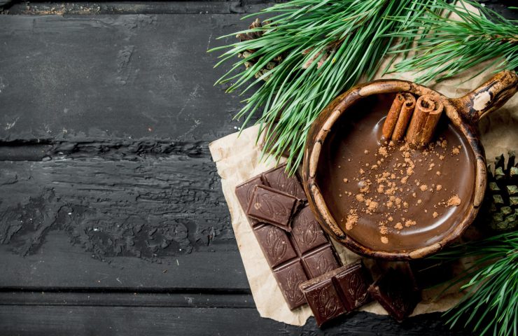 Hot chocolate with cinnamon sticks. On black rustic background.